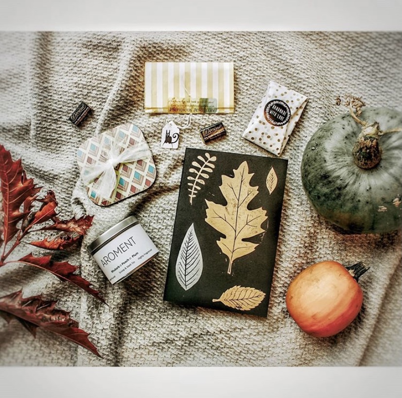 Lots of stocking filler type gifts laid out on a blanket, surrounded by foliage and pumpkins.