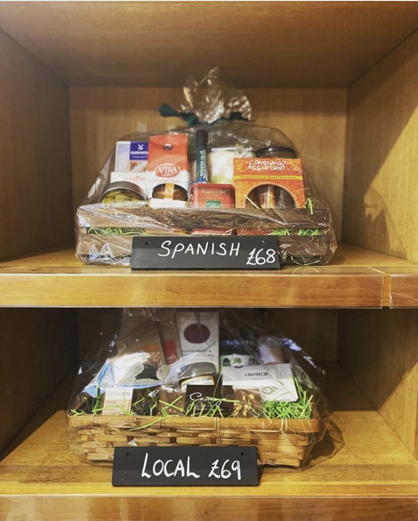 Two food hampers, beautifully wrapped on a shelf with price and name labels. 