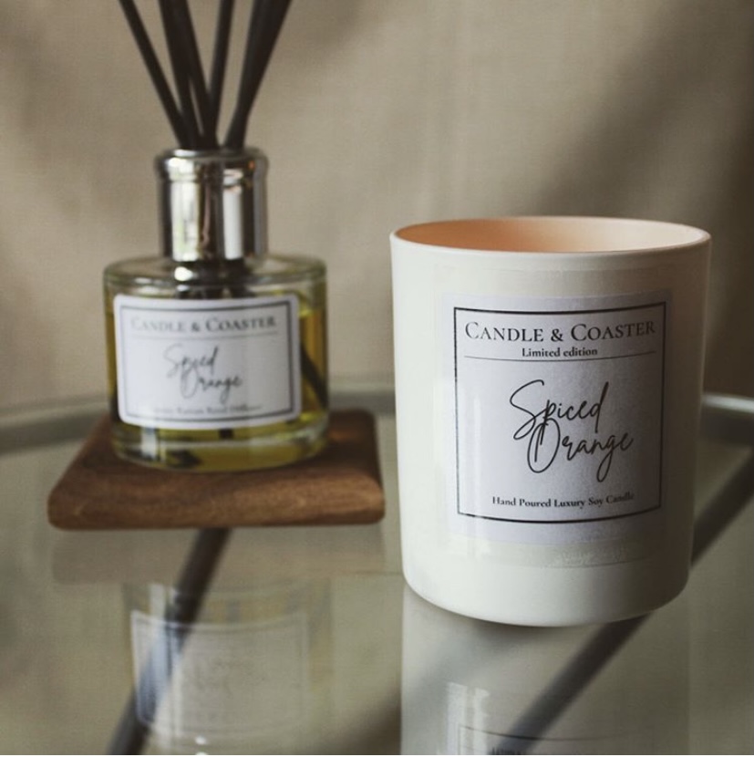 A candle and reed diffuser on a glass tabletop.