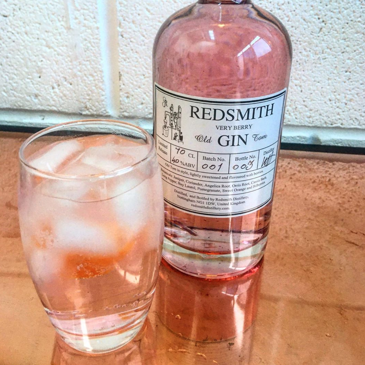 A bottle of gin with a glass filled with ice and gin and tonic beside it on a tabletop.